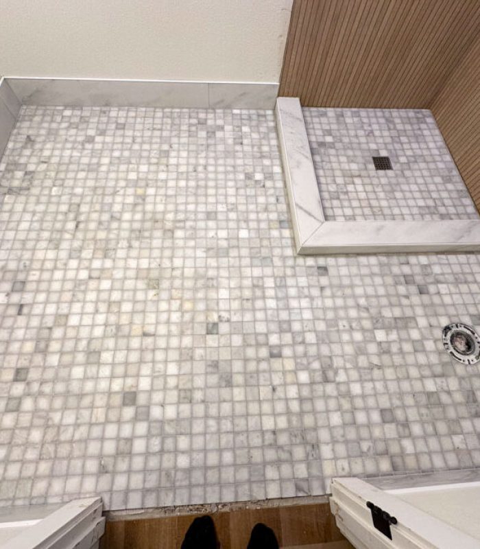 A luxurious walk-in shower with a combination of white marble tiles and a mosaic tile floor, offering a spa-like atmosphere.